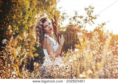 Portrait of a beautiful attractive lady of a young slender brunette girl with long dress walking through a green park with flowers at sunset lifestyle outdoor.