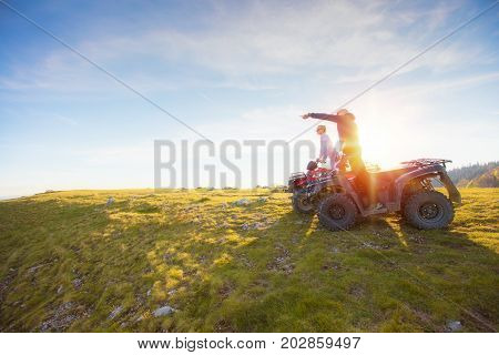 Rear view of young pair near atv. Man is showing something in distance to her girlfriend. Blurred autumn landscape mighty mountains and forests on background