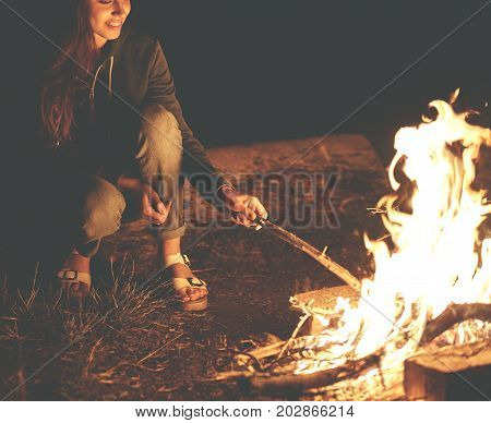 Young woman in geans and hoodie in the mountains. Young woman with fire on mountain at sunset. Girl standing near a fireplace