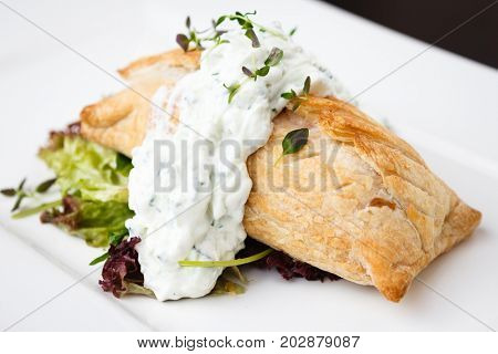 Traditional russian pie - coulibiac. Baked puff pastry filled with smoked salmon, served with sour cream sauce