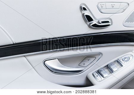Door handle with Power seat contol buttons of a luxury passenger car. White leather interior of the luxury modern car. Modern car interior details