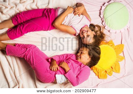 Children With Happy Faces Lie Close On Pink Blanket Background.