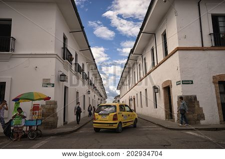 July 6, 2017 Popayan, Colombia: a yellow taxi turns into a narrow street flanked by white wash historic colonial buildings