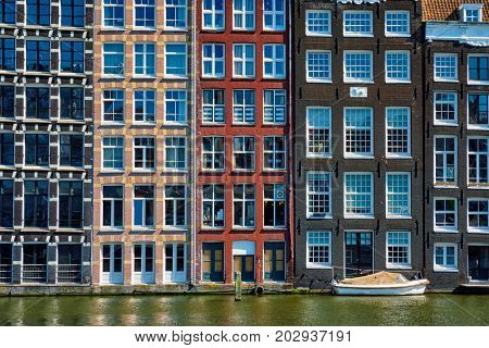 Row of typical houses and boat on Amsterdam canal  Damrak with reflection. Amsterdam, Netherlands
