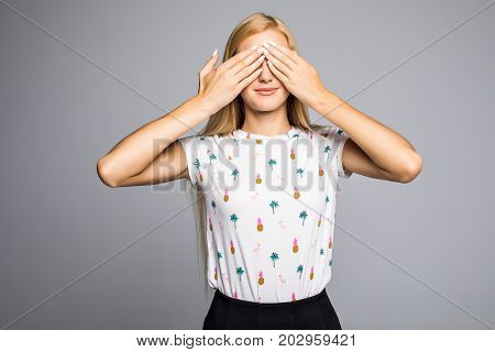Portrait Of Young Scared Woman Covering Eyes With Hands While Standing Against Gray Studio Backgroun