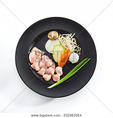 Teppanyaki Japanese and Korean Grill Food - Chicken with vegetables with fresh herbs and mushrooms on black plate on white isolated background. Preparation of raw food for frying on teppan. Top View