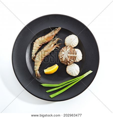 Teppanyaki Japanese and Korean Grill Food - 16/20 Shrimp with mushrooms with an lemon slice and fresh herbs on black plate on white isolated background. Preparation of raw food for frying on teppan