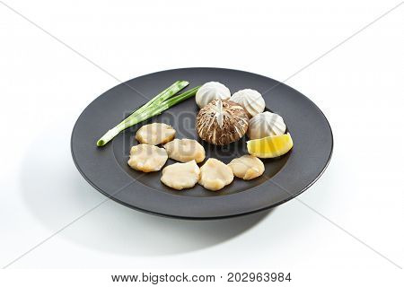 Teppanyaki Japanese and Korean Grill Food - Sea scallop with mushrooms with lemon slice and fresh herbs on  black plate on white isolated background. Raw food preparation for frying on teppan