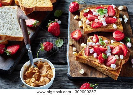 Sandwiches Of Toasted Bread With Peanut Butter, Sliced Strawberries And Marshmallow On A Wooden Cutt