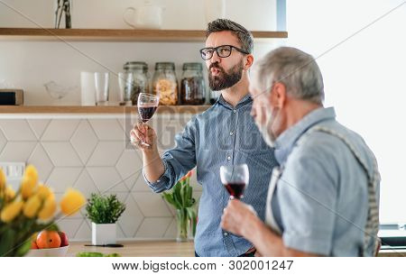 An Adult Hipster Son And Senior Father Indoors In Kithcen At Home, Tasting Wine.