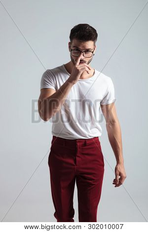 Determined man walking forward and adjusting his glasses while wearing red pants and a a white t-shirt on gray studio background