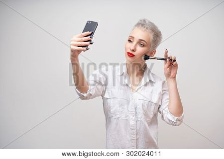 Studio Portrait Of Beautiful Trendy Girl With Short Hair Taking Selfie Via Cell Phone Over White Iso