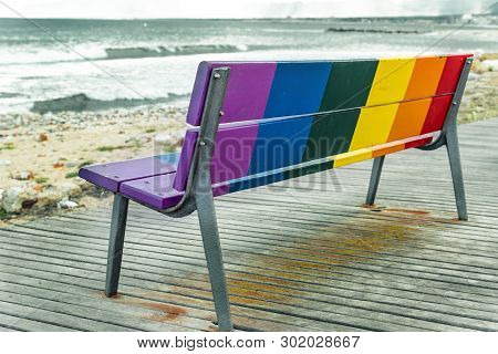 Rainbow Lgbt Pride Flag Painted On A Wooden Bench On The Beach With The Sea In The Background.