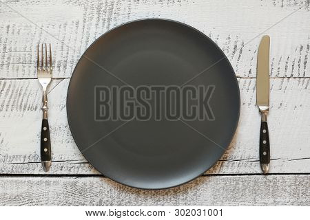 Table Place Setting With Black Plate On White Wooden Table. Top View.