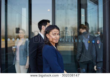 Content Beautiful Young Black Woman In Dark Blue Jacket Looking At Camera While Coming In Office Bui