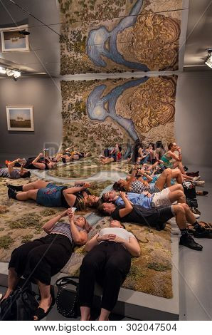 Melbourne, Australia - March 17, 2018: Visitors Resting On The Hand Tufted Wool Rug Entitled Santa C