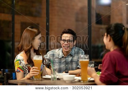 Group Of Asian Friends Hanging Out Talking Together Drink Pint Glass Of Beer On Friday Night In Rela