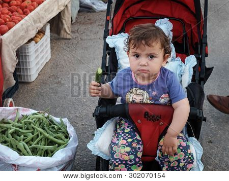 Tasucu, Mersin Province, Turkey - May 2019. Baby In The Carriage Eats A Cucumber