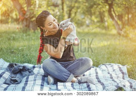 Asian Woman Took On Picnic Little Gray Bunny. Happy Girl Hugging Bunny In Green Summer Forest. Girl 