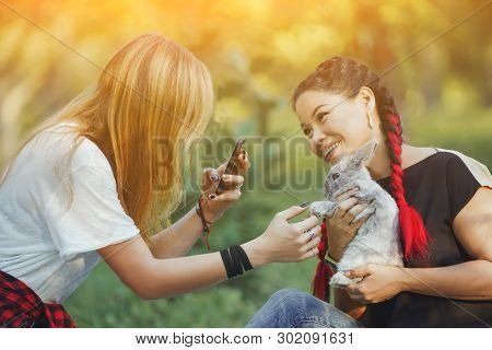 Two Girl With Rabbit On Nature Taking A Photo Of Rabbit. Little Pretty Bunny On Hands Of Asian Girl 