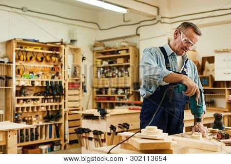 Waist Up Portrait Of Senior Carpenter Drilling Wood While Working In Joinery, Copy Space