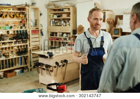 Portrait Of Young Carpenter Talking To Senior Worker During Coffee Break In Workshop, Copy Space