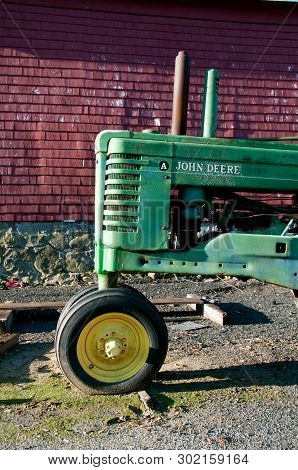 Rowley, Massachusetts, April 28, 2019: The Old A John Deere Tractor Parked In Front Of A Red Barn Ii
