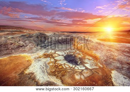 Mudpots in the geothermal area Hverir, Iceland. The area around the boiling mud is multicolored and cracked. Sunset time