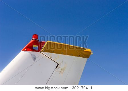 Tail Fin, Rudder And Beacon Lights, Small Single Engine Airplane With Old Paint And Bright Blue Sky.