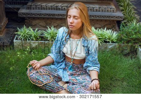 Beautiful Young Woman Sitting On The Grass In The Lotus Position With Eyes Closed And Meditating.