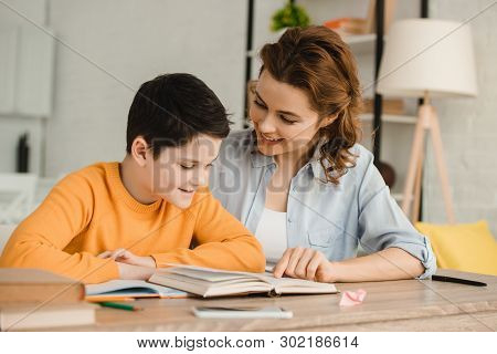 Smiling Mother Helping Adorable Son Doing Schoolwork At Home