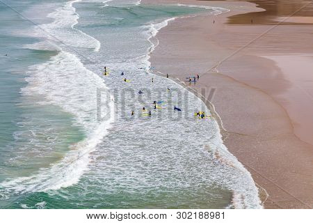 Surfers In The Waves Off Mawgan Porth Beach, Cornwall, Uk