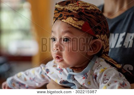 A Portrait Of A 3-month-old Baby Showing A Smile And Wearing Blangkon. Blangkon Is A Typical Head Co