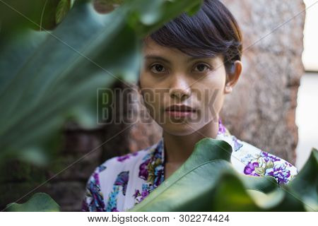 A Portrait Of A Beautiful Short-haired Woman With A Flower On His Ear. She Is Wearing A Bali Dress W