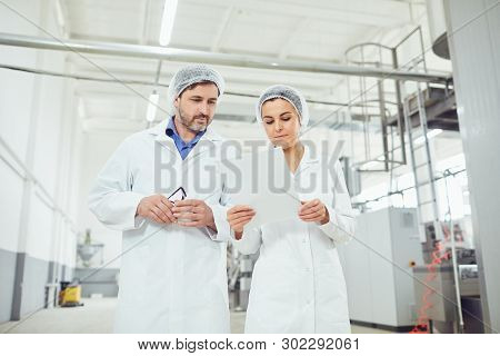 Two Technologists In Lab Coats And Masks At The Factory.