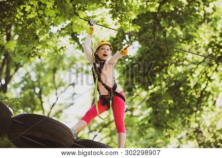 Little Girl Having Fun At Adventure Park. Carefree Childhood. Happy Little Girl Climbing In The Tree