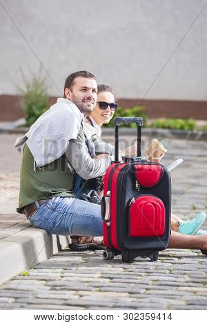 Happy Couple Traveling Around City. Having Lunch With Sandwiches. Sitting On Floow With Luggage And 
