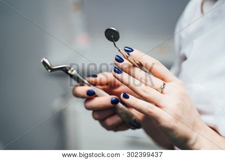Hands Of A Stomatologist With Blue Nails Are Holding Stainles Instruments In Clinic. Medical Equipme