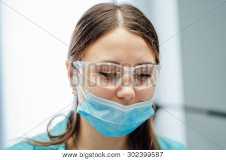 Portrait Of A Young Female Dentist In Surgical Mask And Safety Glasses. Beauty Face Of A Doctor Or N