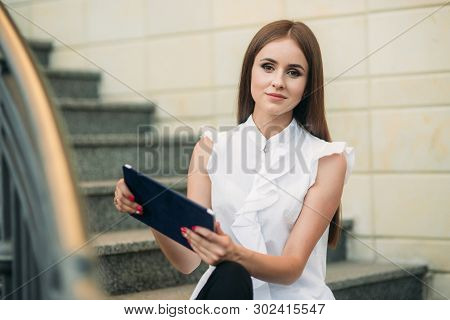 Young And Attractive Female Sittind On The Stairs And Use Tablet. Woman Play Online Games On Tablet