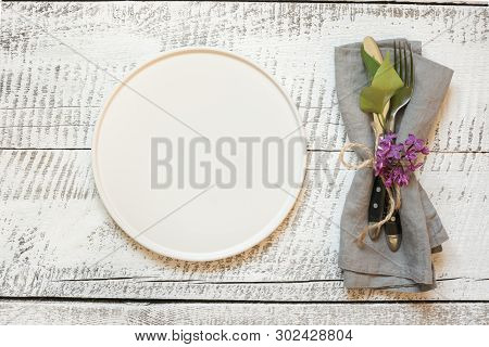 Table Place Setting With White Plate, Lilac Flowers On White Wooden Table. View Vrom Above. Horizont