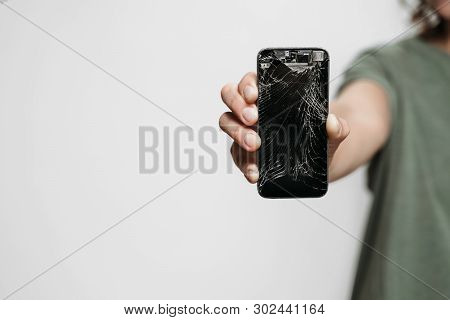 Close Up, Hand Holding Broken Smartphone With Damaged Screen Isolated On Gray Background. Free Copy 