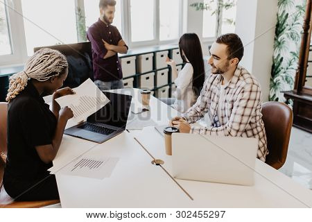 Group Of Young Business People Working, Communicating While Sitting At The Office Desk Together With