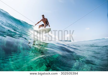 HIMMAFUSHI / MALDIVES - MARCH 08, 2019: Young man surfs the glassy ocean wave at sunny day