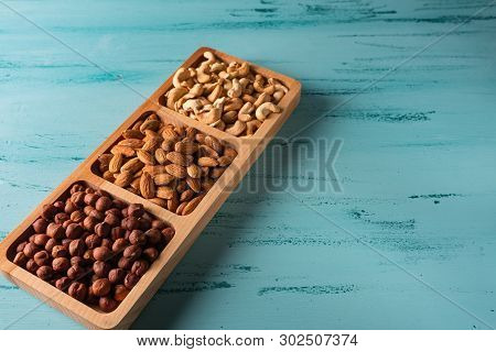 Compartmental Dish With Nuts On Blue Wooden Table. Cashew, Hazelnut, Almond.
