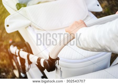 Woman Strolling With White Baby-carriage. Close Up Of Female Hand In White Jacket With Baby-carriage