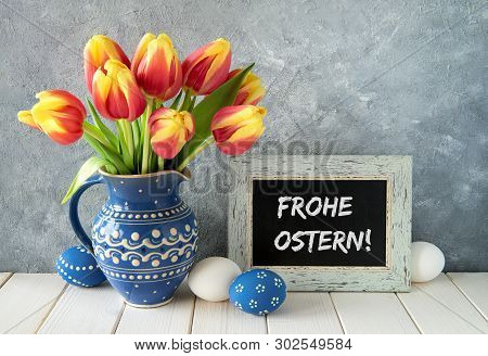 Red-yellow Tulips In Blue Ceramic Pitcher With Easter Eggs And A Blackboard On Gray Background. Text