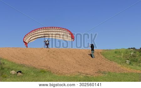 Female Pilot Landing With A Paraglider In The Field With A Blue Sky Background