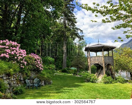 A Beautiful Wooden Pagoda On Top Of A Tree Stump Surrounded By Pink Flowers And Tall Evergreen Trees