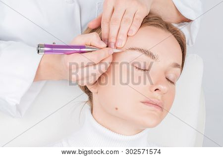 Microblading Eyebrows. Cosmetologist Making Permanent Makeup. Attractive Woman Getting Facial Care A